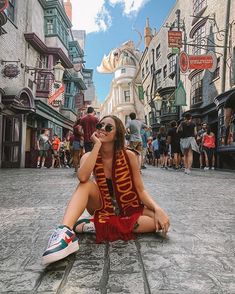 a woman sitting on the ground in front of a street with buildings and people walking around