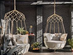 two hanging chairs in front of a brick wall with potted plants on the other side