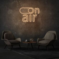 two chairs and a table in front of a neon sign that says on air above them