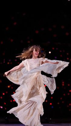 a woman in a white dress is dancing on stage with her arms spread out to the side