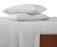 two pillows are stacked on top of each other in front of a bed with white sheets