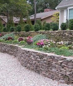 a stone wall and flower bed in front of a house