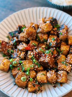 a white plate topped with tofu covered in sesame seeds and garnished with green onions