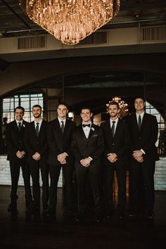 a group of men standing next to each other in front of a chandelier