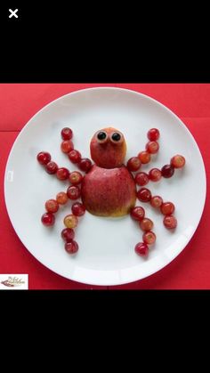 a white plate topped with grapes and an apple shaped like a spider