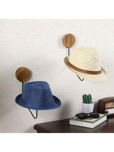 three hats are hanging on the wall next to a desk with a book and cactus