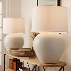 two white vases sitting on top of a wooden shelf next to a lamp and basket