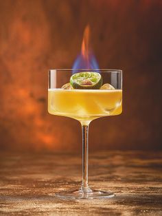 a glass filled with yellow liquid sitting on top of a table next to a fire