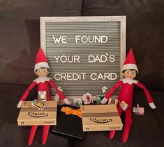 two elfs are sitting next to each other with boxes on the couch and a sign that says, we found your dad's credit card