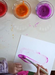 a child is painting with different colors of paint on paper and watercolor pencils