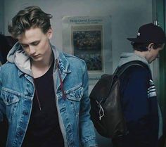 two young men are standing next to each other in the hallway, looking at their cell phones