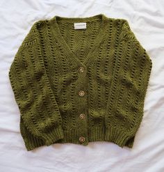 a green knitted sweater laying on top of a white bed sheet with buttons in the middle