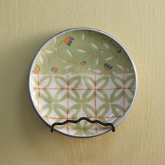 a green and orange plate hanging on the wall next to a yellow wall with an ornament