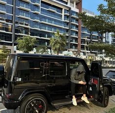 a man sitting in the open door of a black jeep parked next to a tall building