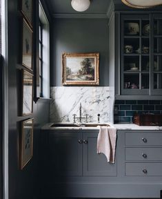 a kitchen with gray cabinets and marble counter tops, along with a painting on the wall