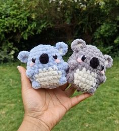 two small crocheted koalas sitting on top of each other in the grass