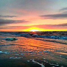 the sun is setting over the ocean with ice flakes on the beach and waves coming in