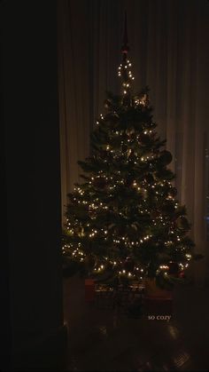 a lit christmas tree in the corner of a room