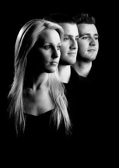 three people standing in front of a black background with one person looking at the camera