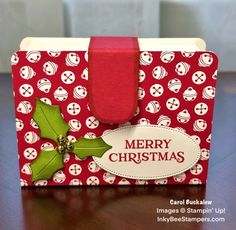 a red and white christmas card on a wooden table with a holly berry tag attached to it