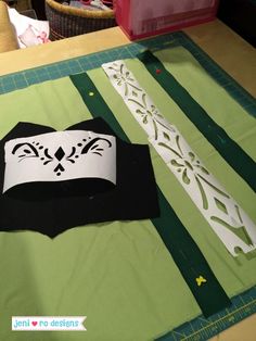 paper cutouts are sitting on top of a green and white table cloth with scissors next to it