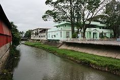 a river running through a lush green countryside next to tall buildings with red roofing