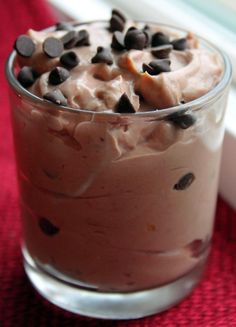 a dessert in a glass with chocolate chips and cream toppings on top, sitting on a red table cloth