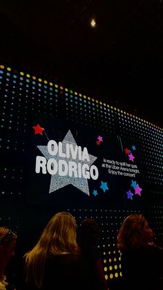 a group of people standing in front of a large screen with the name olvia rodrigo on it