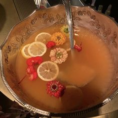 a metal bowl filled with liquid and lemons on top of a table next to flowers