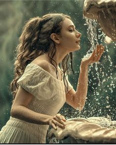 a woman in white dress standing under a fountain with water pouring out of her hands