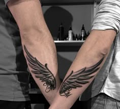 two people holding hands with tattoos on their arms and one has an angel wing tattoo