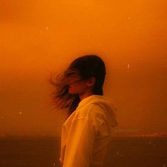 a woman standing in front of an orange sky with her hair blowing in the wind