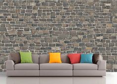 a gray couch with colorful pillows in front of a stone wall