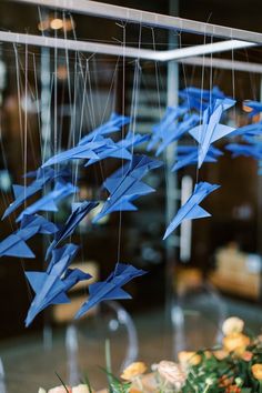 blue origami birds hanging from strings in front of a glass case filled with flowers