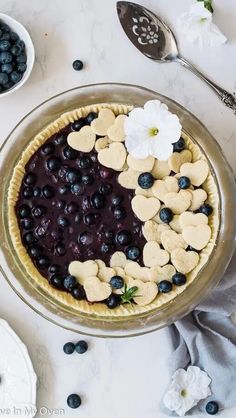 a pie with blueberries and heart shaped cookies in it on a table next to spoons