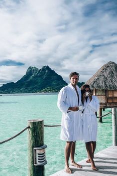 a man and woman standing on a dock next to the ocean