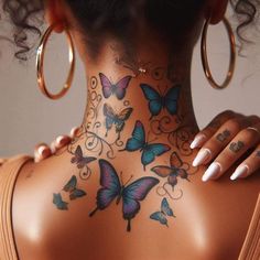 the back of a woman's neck with butterflies painted on her body and in gold hoop earrings