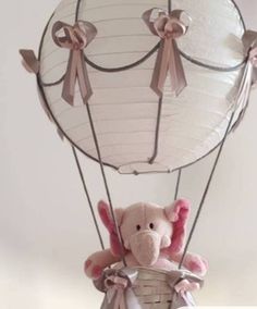 a stuffed elephant in a basket attached to a hot air balloon with ribbons on it