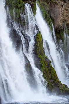 a waterfall with green moss growing on the side and water running down it's sides