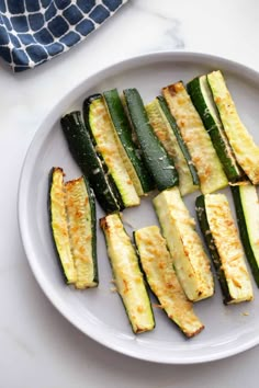 cooked zucchini on a white plate next to a blue and white dish towel