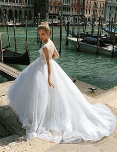 a woman in a white wedding dress standing on a dock next to some water and boats