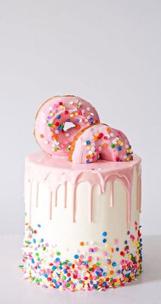 a pink frosted cake with sprinkles and two donuts on top