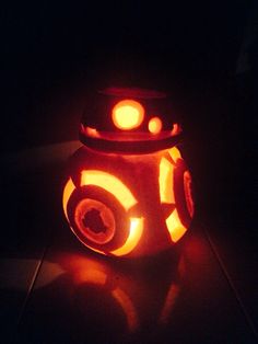 a pumpkin carved to look like a droid with glowing eyes and ears, sitting in the dark