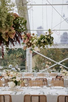 the tables are set up for an event with flowers and greenery hanging from the ceiling