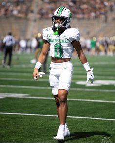 a football player is walking on the field with his hands in his pockets while wearing white and green