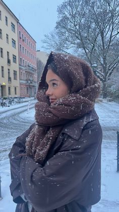 a woman standing in the snow with her arms wrapped around her head and looking off into the distance