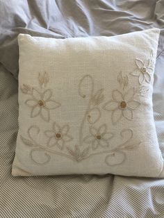 a white pillow with embroidered flowers on it sitting on top of a bed covered in sheets