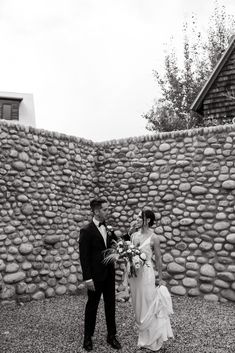 a bride and groom standing in front of a stone wall