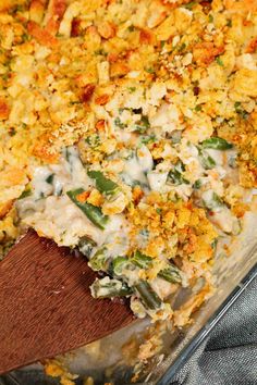 a casserole dish filled with green beans, cheese and other toppings on a wooden spatula