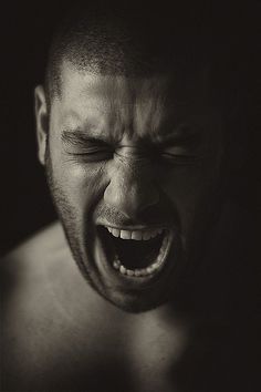 a shirtless man with his eyes closed and mouth wide open, yelling into the camera